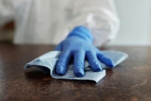 A hand wearing a blue glove wipes a surface with a cloth, emphasizing hygiene and cleanliness.